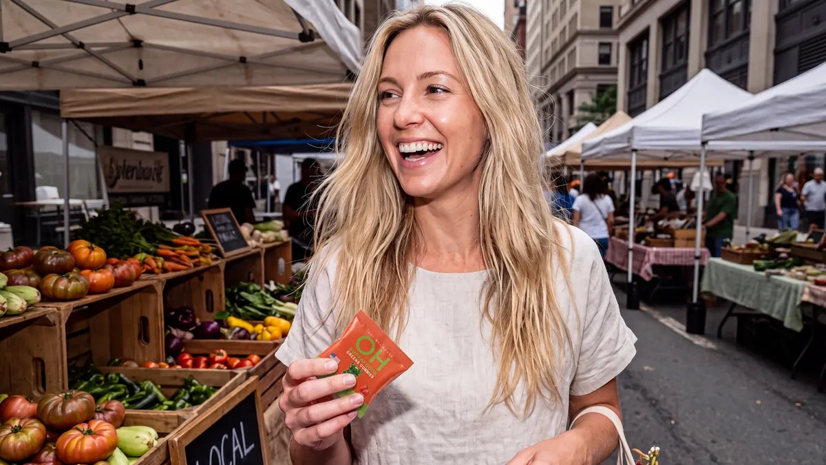 A smiling woman at a farmers market holding a Superfood Greens Gummies pack