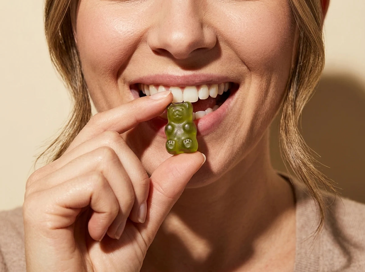 A smiling woman biting a green strawberry gummy