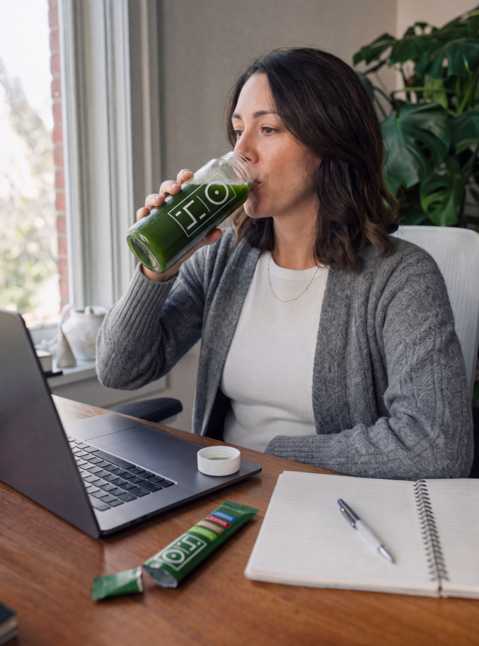 A woman at her desk sipping Superfood Greens from the bottle