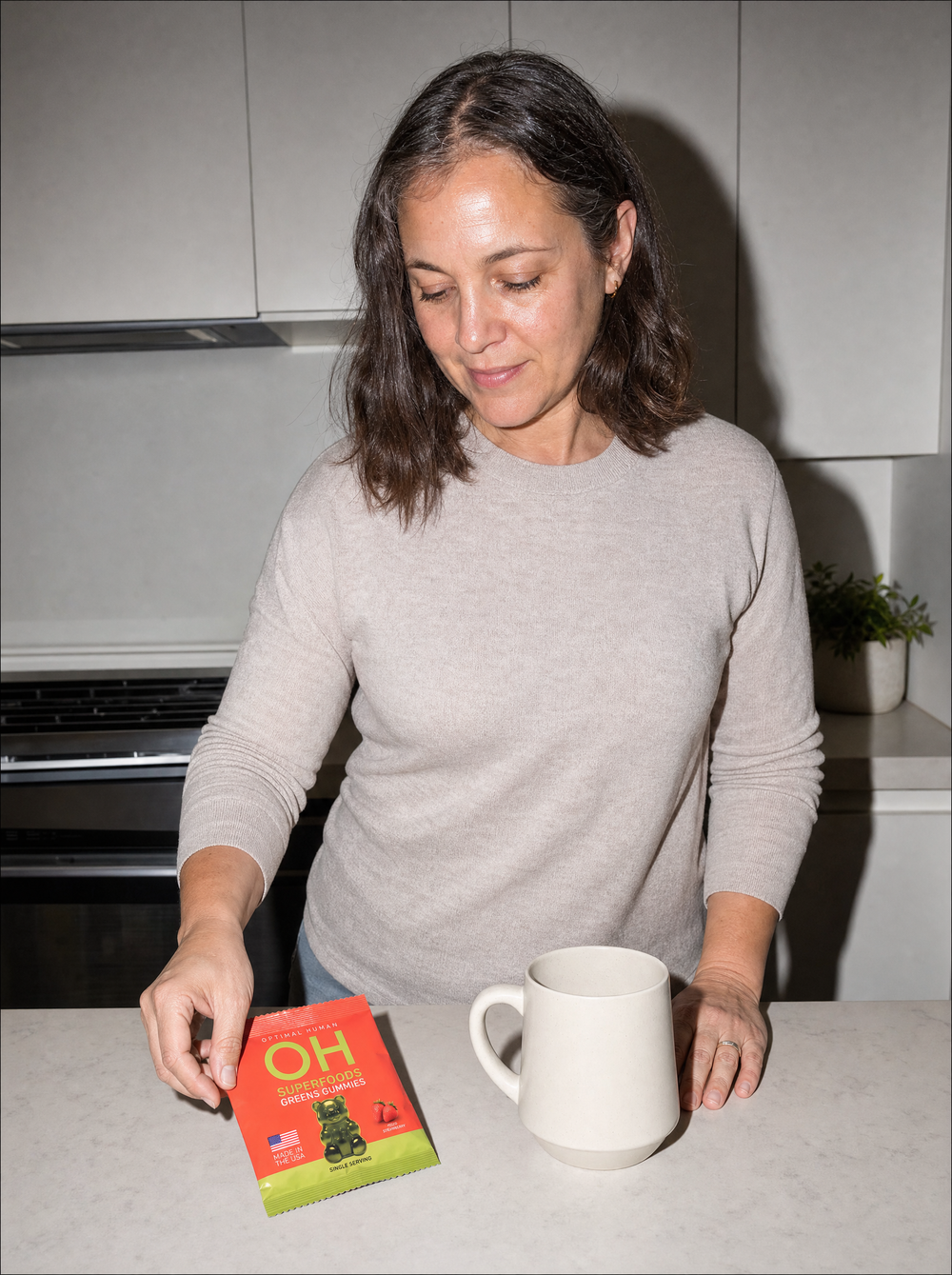 A woman reaching for a pack of greens gummies on a kitchen counter in morning light
