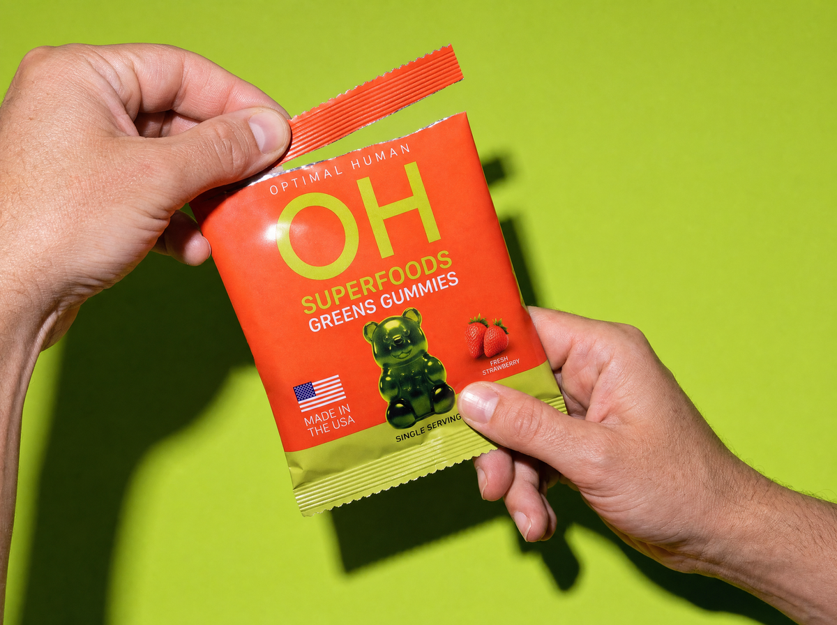 Two hands tearing open a single-serve pack of greens gummies
