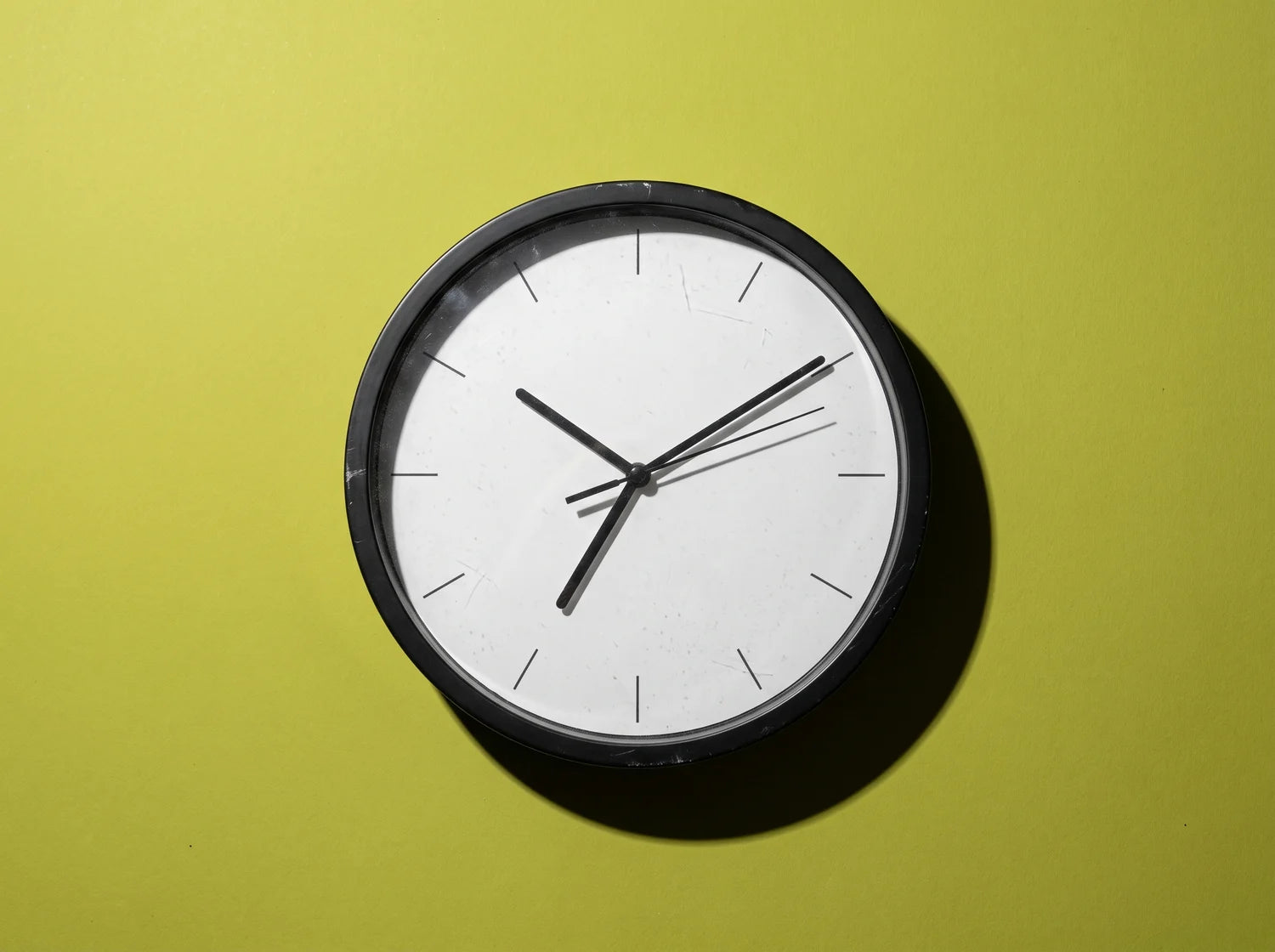 A plain round wall clock lying face up in the early morning, studio still life on lime paper