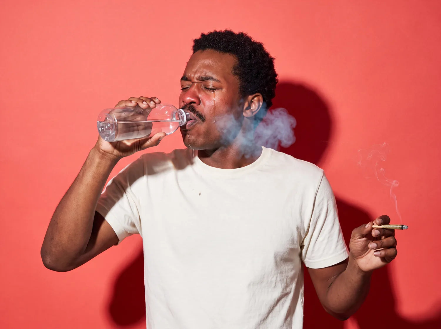 A man with his eyes squeezed shut, gulping from a big water bottle, on coral paper