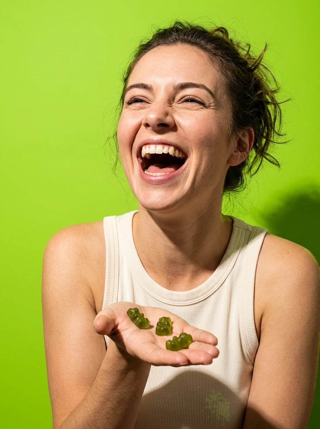A woman laughing with green gummies in her open hand