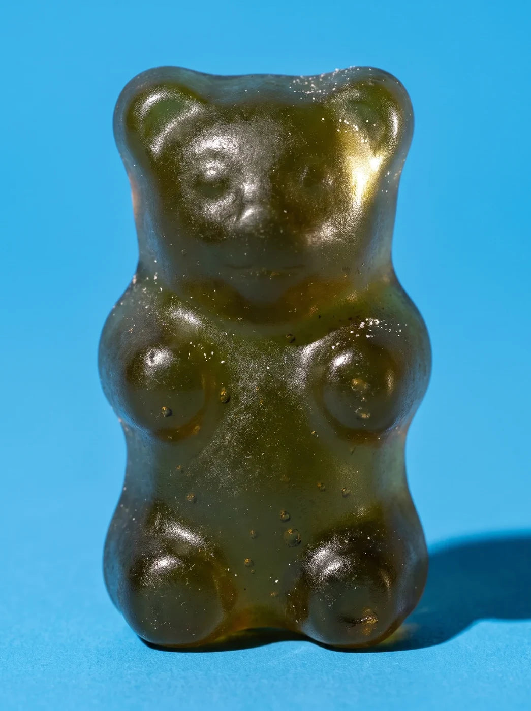 One green strawberry gummy bear on a sky-blue background