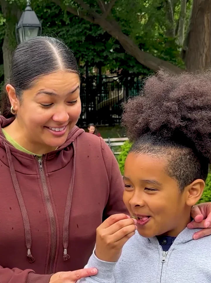 A mom smiling as her son eats a green gummy in the park