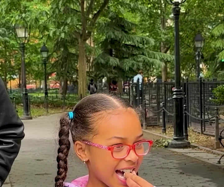 A girl in pink glasses tasting a green gummy