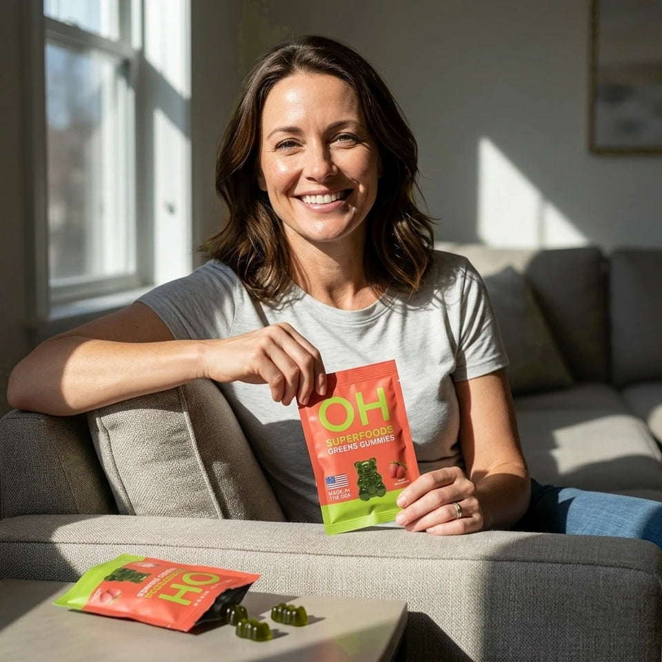 A smiling woman on her sofa opening a Superfood Greens Gummies pack