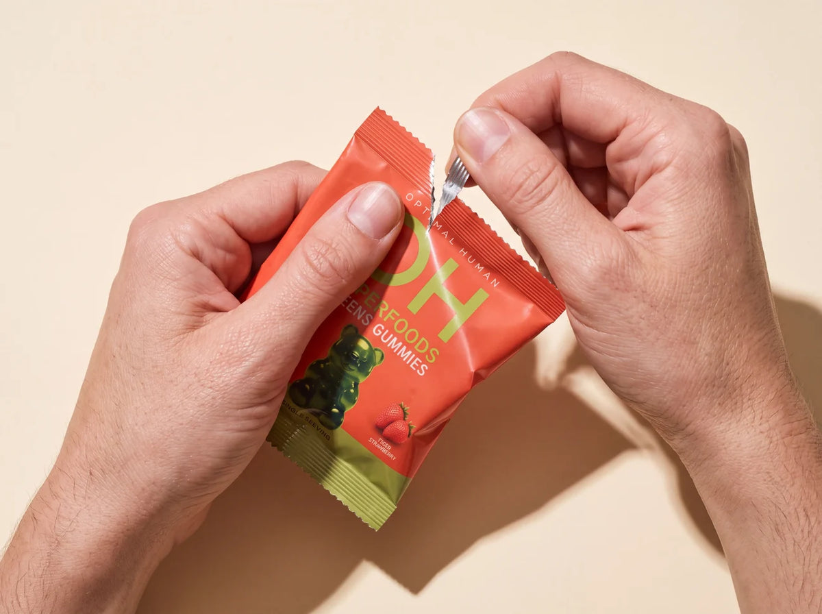 Hands tearing open an Optimal Human Superfood Greens Gummies pack